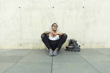 Tattooed young man with roller skates sitting on ground having fun - JPTF00054