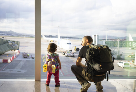 Vater und Tochter mit Rucksäcken am Flughafen und Blick auf die Flugzeuge, lizenzfreies Stockfoto