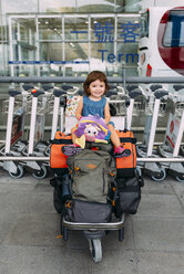 Ein kleines Mädchen sitzt oben auf dem Gepäck in einem Trolley am Flughafen - GEMF02434