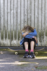 Mädchen sitzt auf ihrem Skateboard im Freien und versteckt ihr Gesicht - JFEF00908