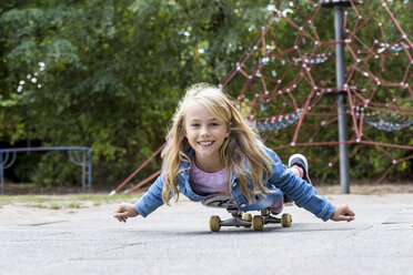 Porträt eines lächelnden blonden Mädchens mit Skateboard auf einem Spielplatz - JFEF00911