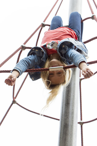 Blond girl hanging upside down on jungle gym at playground stock photo