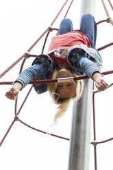 Blondes Mädchen hängt kopfüber am Klettergerüst auf dem Spielplatz - JFEF00914