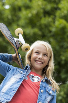 Porträt eines glücklichen blonden Mädchens mit Skateboard auf der Schulter - JFEF00917