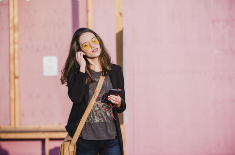 Junge Frau mit Mobiltelefon und Kopfhörern, die eine farbige Sonnenbrille trägt, lizenzfreies Stockfoto