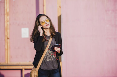 Young woman with cell phone and earphones wearing coloured sunglasses - UUF15644
