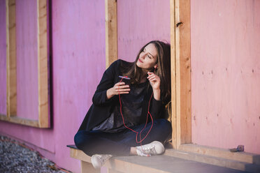 Young woman sitting outdoors listening to music - UUF15647