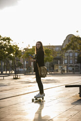 Junge Frau mit Handy fährt Longboard in der Stadt - UUF15648