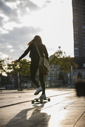 Rückansicht einer jungen Frau auf einem Longboard in der Stadt - UUF15663