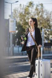 Young woman with luggage at tram station on the move - UUF15671