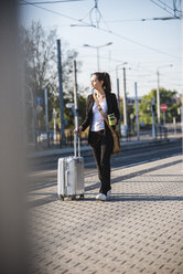 Junge Frau mit Gepäck an der Straßenbahnhaltestelle unterwegs - UUF15672