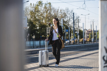 Junge Frau mit Gepäck an der Straßenbahnhaltestelle unterwegs - UUF15673