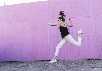 Exuberant young woman jumping in front of pink wall - UUF15688