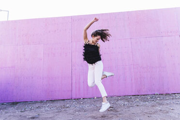 Überschwängliche junge Frau, die vor einer rosa Wand springt - UUF15691