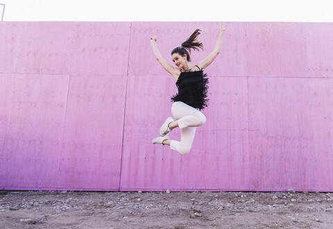 Überschwängliche junge Frau, die vor einer rosa Wand springt, lizenzfreies Stockfoto