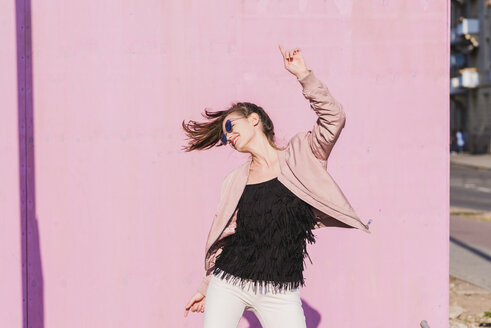 Happy young woman moving in front of pink wall - UUF15703