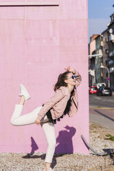 Glückliche junge Frau, die sich vor einer rosa Wand bewegt - UUF15705