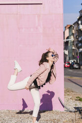 Happy young woman moving in front of pink wall - UUF15705