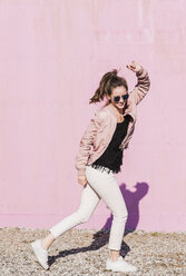 Glückliche junge Frau, die sich vor einer rosa Wand bewegt - UUF15706