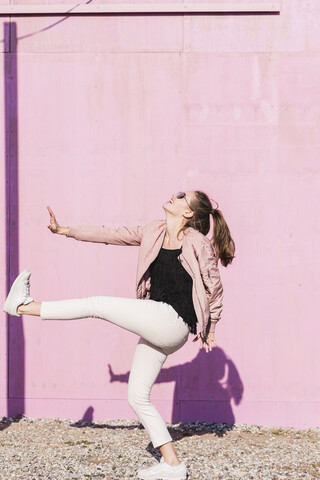 Happy young woman moving in front of pink wall stock photo