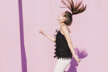 Happy young woman moving in front of pink wall - UUF15708