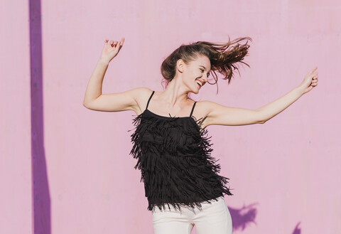 Glückliche junge Frau, die sich vor einer rosa Wand bewegt, lizenzfreies Stockfoto