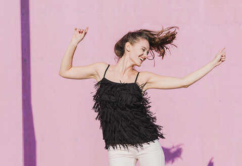 Happy young woman moving in front of pink wall - UUF15711