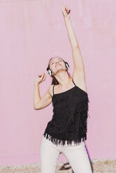 Happy young woman wearing headphones dancing in front of pink wall - UUF15722