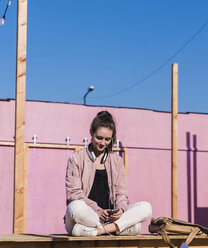 Young woman sitting on platform using cell phone - UUF15729