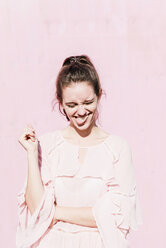 Porträt einer jungen Frau, die vor einer rosa Wand Grimassen schneidet - UUF15736