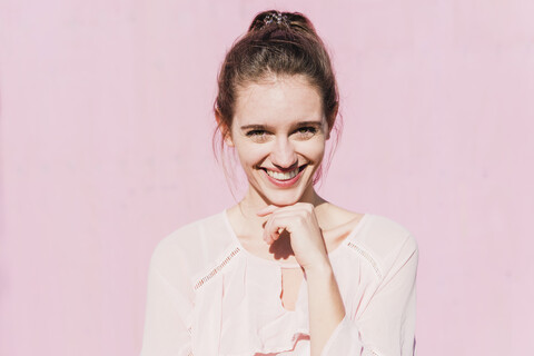 Porträt einer lächelnden jungen Frau vor einer rosa Wand, lizenzfreies Stockfoto