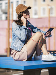 Relaxed young woman sitting on table tennis table listening to music - UUF15754