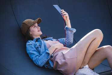 Young woman lying outdoors holding cell phone - UUF15755