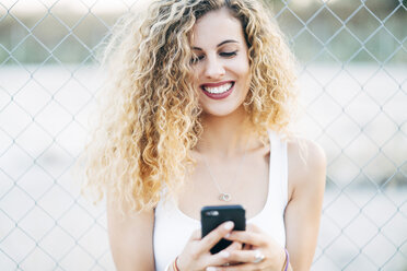 Porträt einer lachenden blonden jungen Frau, die auf ihr Mobiltelefon schaut - OCMF00014