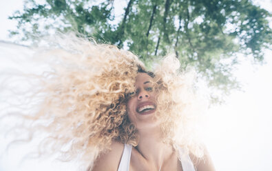 Porträt einer glücklichen jungen Frau mit blonden Locken im Gegenlicht - OCMF00020