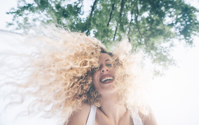 Portrait of happy young woman with blond ringlets at backlight - OCMF00020