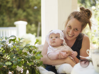 Porträt einer lächelnden Mutter mit einem kleinen Mädchen auf dem Schoß auf einer Terrasse sitzend - LAF02118