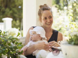 Porträt einer entspannten Mutter mit einem kleinen Mädchen auf dem Schoß auf einer Terrasse sitzend - LAF02121