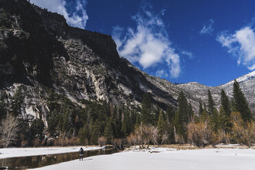 Wanderer, der im Winter im Yosemite-Nationalpark am Fluss steht und Schnee vor den Bergen sieht - CAVF52351