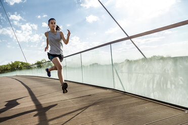 Weibliche Athletin läuft auf Brücke gegen Himmel - CAVF52355