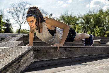 Female athlete doing push-ups on wooden seat against sky - CAVF52357