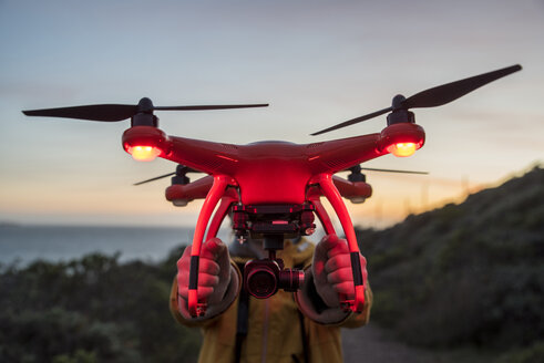 Junge hält beleuchtete Drohne, während er bei Sonnenuntergang gegen den Himmel steht - CAVF52365