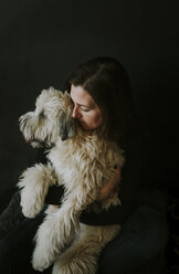 Nahaufnahme einer Frau, die einen Hund umarmt, während sie vor einem schwarzen Hintergrund steht - CAVF52367