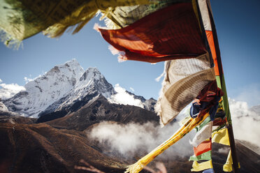 Colorful prayer flags hanging by mountain against blue sky during sunny day - CAVF52379