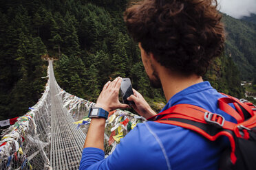 Männlicher Wanderer beim Fotografieren einer Fußgängerbrücke mit dem Smartphone im Sagarmatha-Nationalpark - CAVF52395