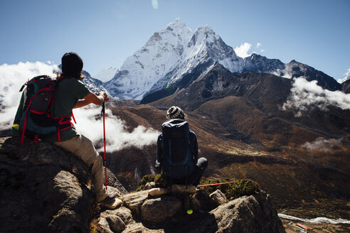 Freunde mit Rucksäcken sitzen auf einem Berg vor blauem Himmel im Sagarmatha-Nationalpark - CAVF52404