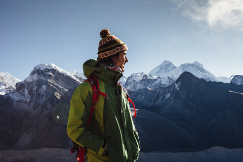 Hiker in warm clothing looking away while standing on mountain against blue sky stock photo
