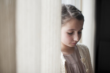 Trauriges Mädchen bei Fenstervorhängen zu Hause - CAVF52439