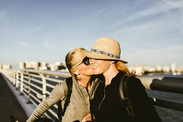 Loving mother kissing daughter on pier against sky in city - CAVF52444