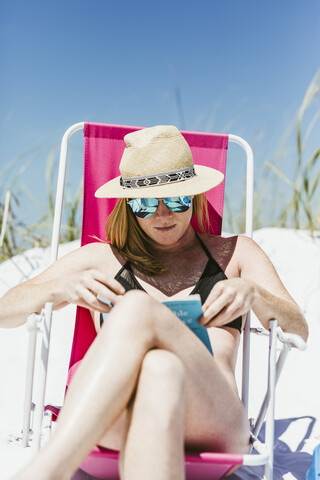 Junge Frau liest ein Buch beim Sonnenbaden am Strand an einem sonnigen Tag, lizenzfreies Stockfoto
